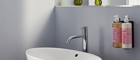 A bathroom with a white sink, a modern faucet, and two bottles of lotion on a shelf.