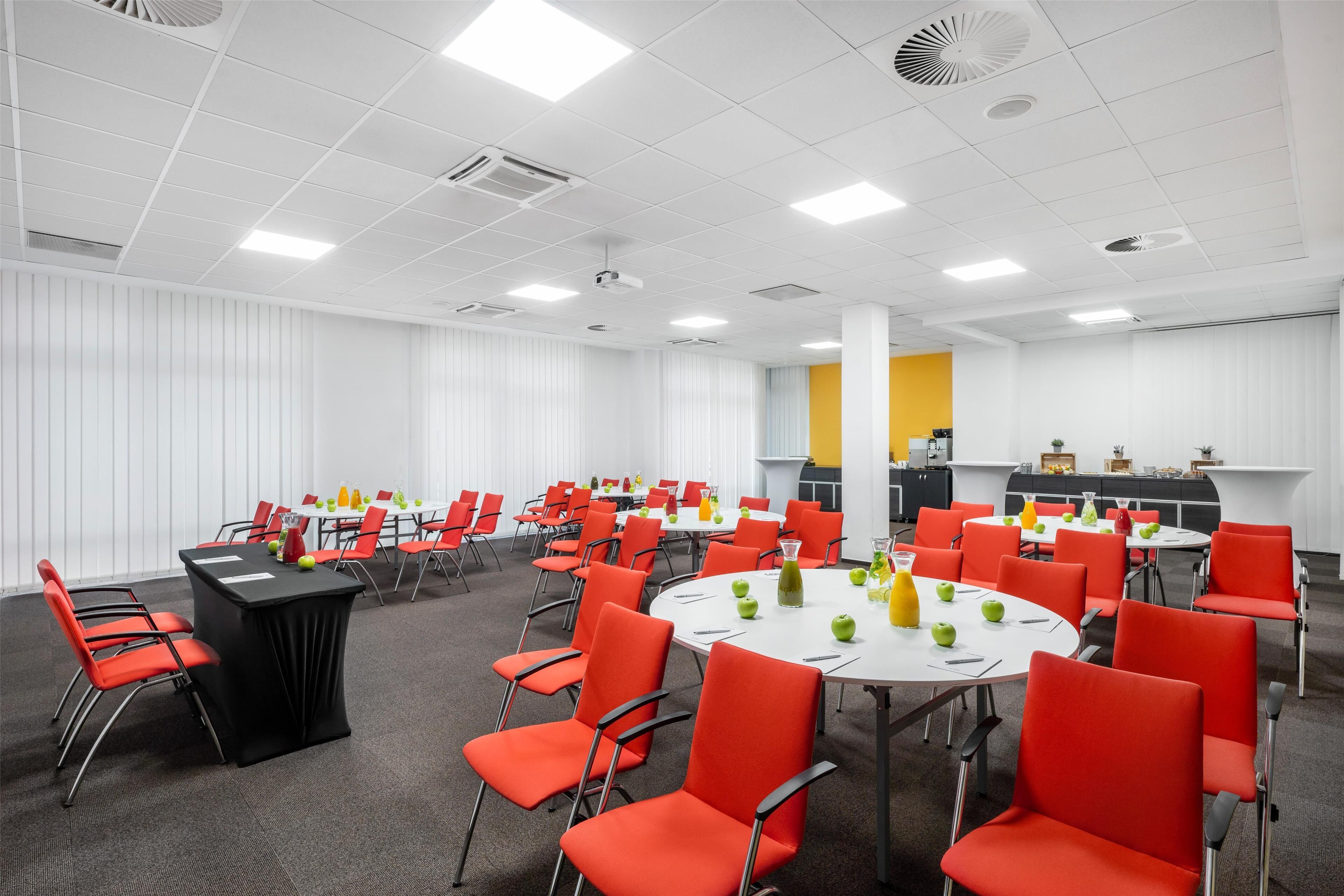 A conference room with multiple tables and red chairs, equipped with projectors and air conditioning units.