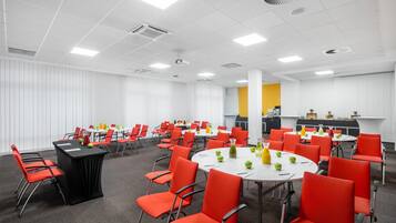 A conference room with multiple tables and red chairs, equipped with projectors and air conditioning units.