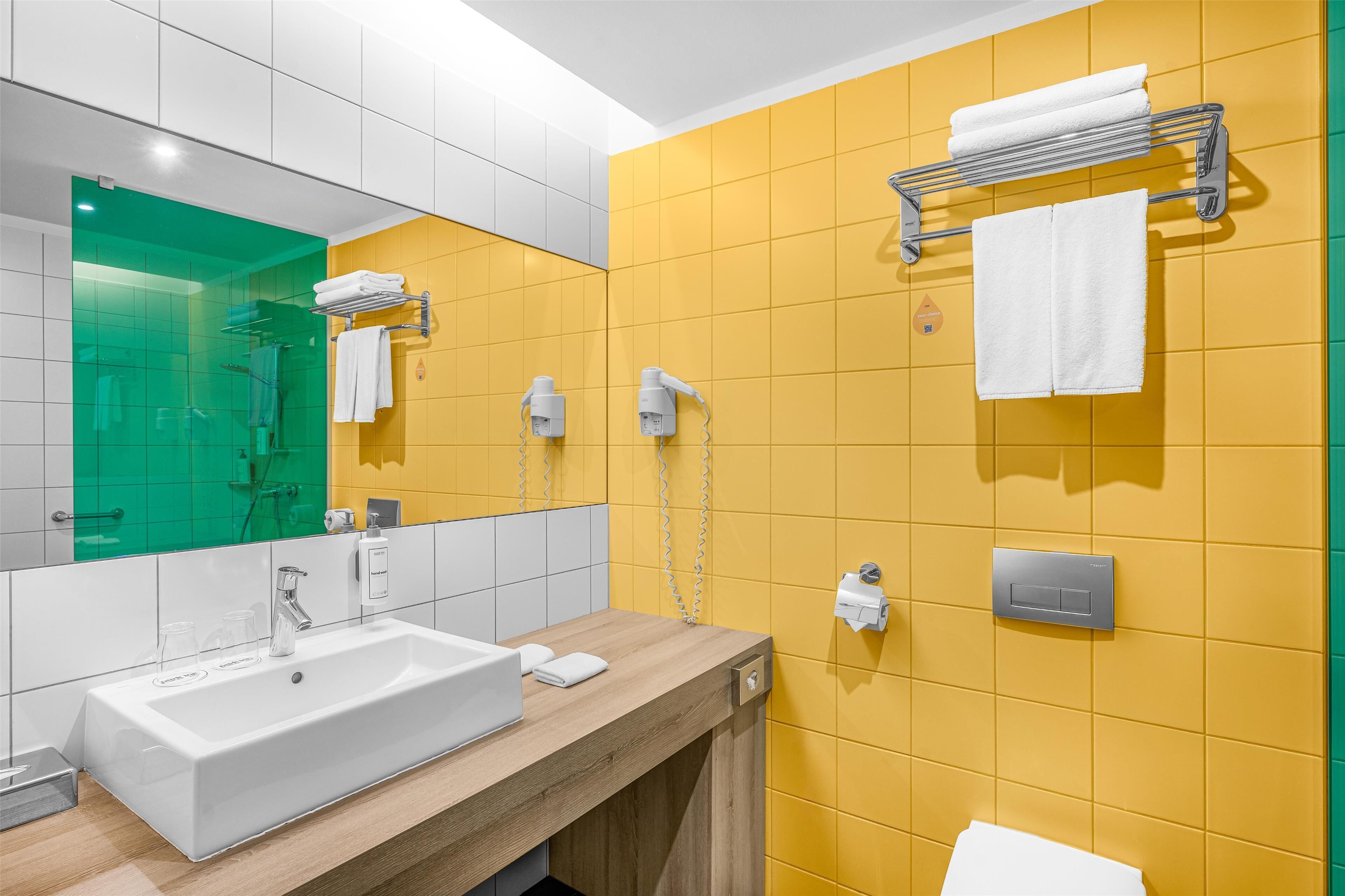Un bany modern amb un lavabo blanc, rajoles grogues, un mirall i una barra de tovalloles.