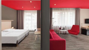 Une chambre d’hôtel avec un lit, un bureau, un canapé rouge et un téléviseur.