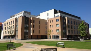A modern building with multiple floors, large windows, and a paved courtyard with benches.