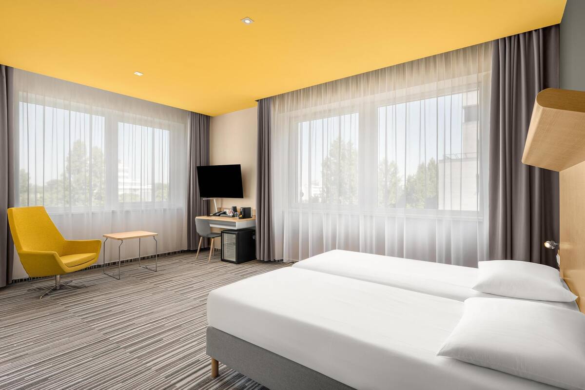 A hotel room with a bed, a desk, a chair, and a TV.