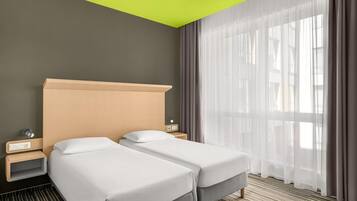 Een hotelkamer met twee bedden, een heldergroen plafond, een groot raam met dunne gordijnen en een gestreept tapijt.