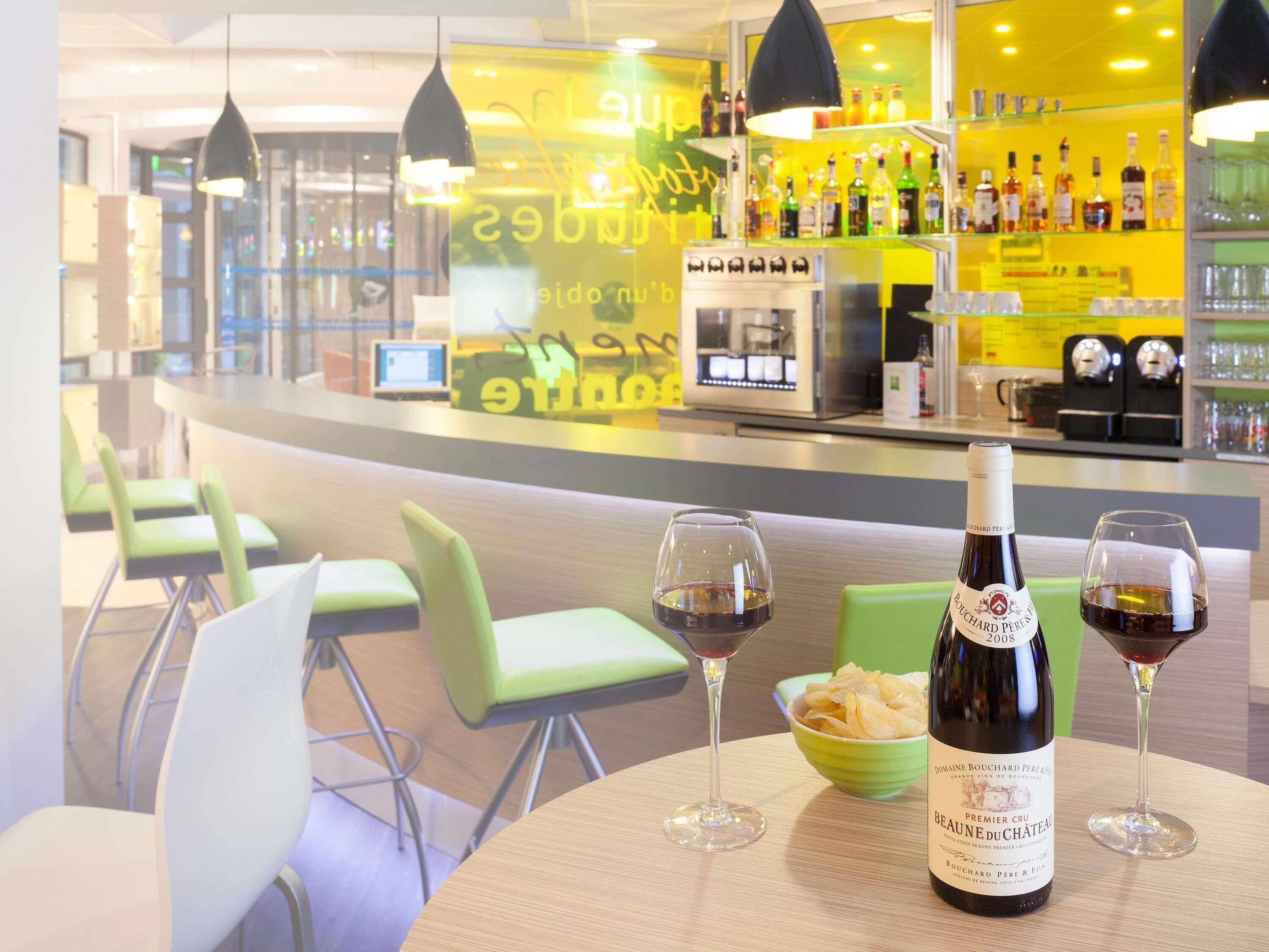 A bar area with a bottle of wine and glasses on a table, bar stools, and a counter with bottles and a coffee machine.