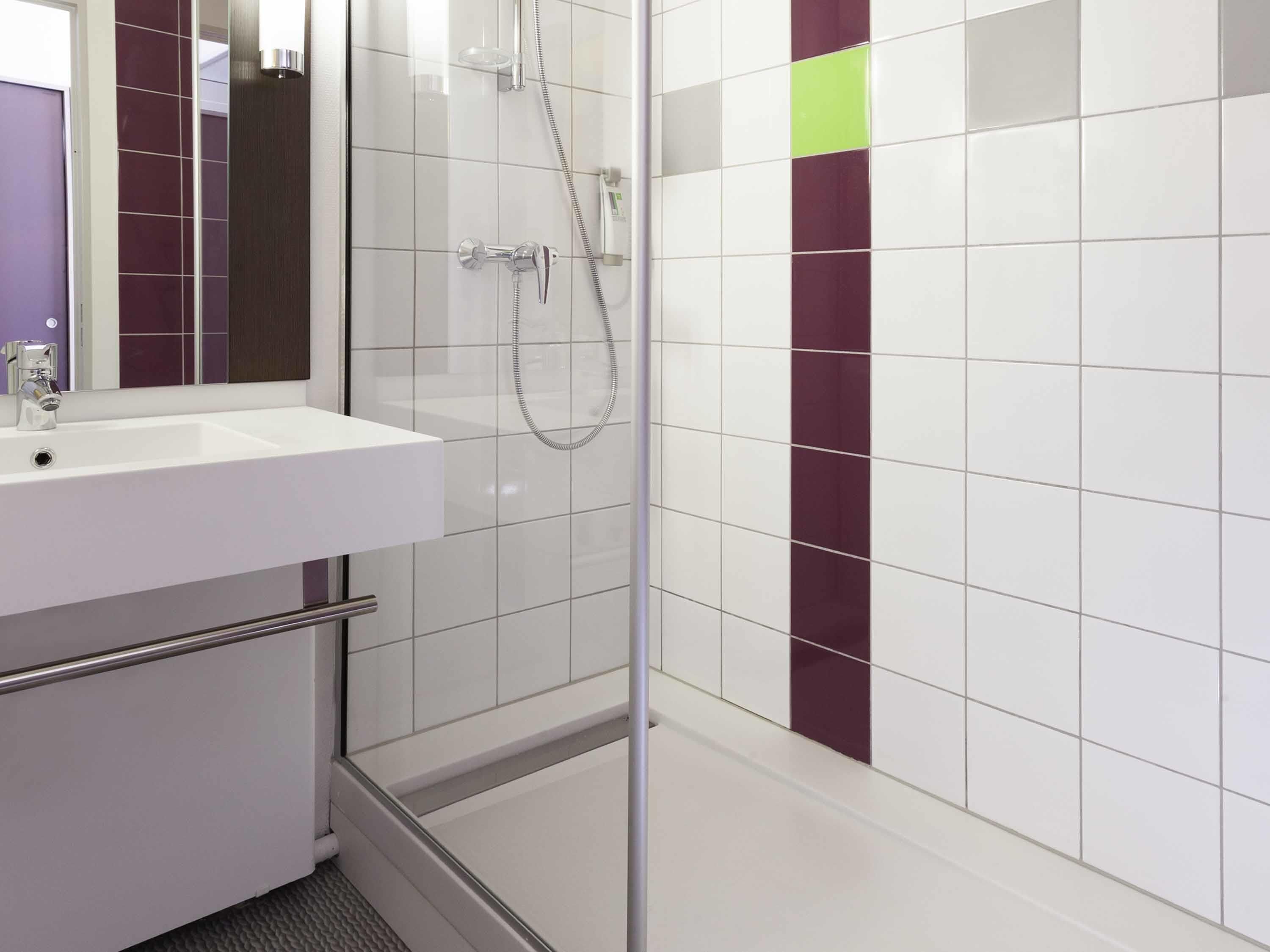 Et moderne badeværelse med en glasbrusekabine, en hvid vask og et spejl.