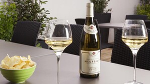 Una botella de vino Meursault, dos copas de vino y un cuenco de patatas fritas sobre una mesa.
