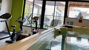 Una piscina interior con equipo de ejercicio y ventanas amplias.