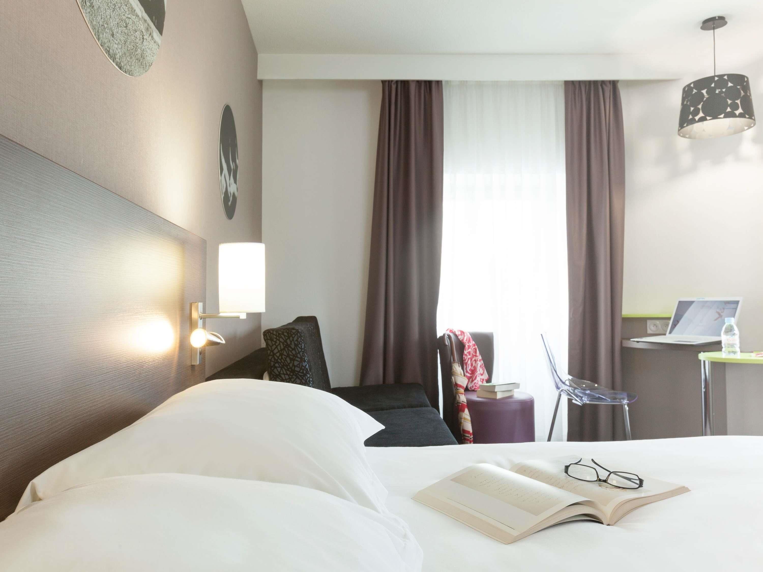 Una camera d'albergo con un letto, una scrivania con un portatile, una sedia e una finestra con tende.