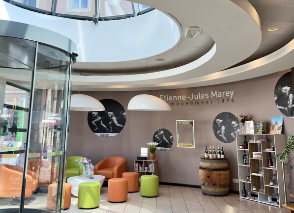 A modern interior with a curved ceiling, seating area with orange and green ottomans, a wooden barrel, and a wall with black and white photographs.