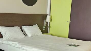 A hotel room with a bed, a headboard, a green and brown wardrobe, and two wall art pieces.