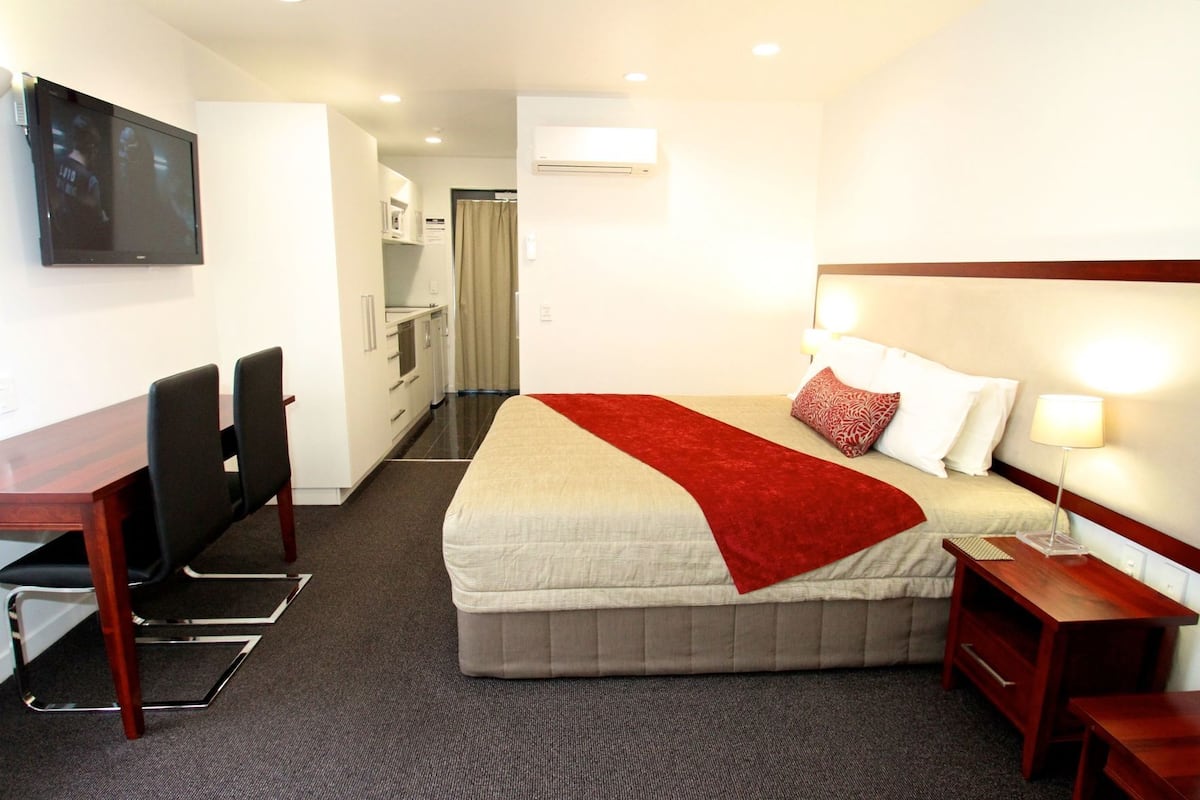 A hotel room with a bed, bedside table, lamp, and a desk with chairs.