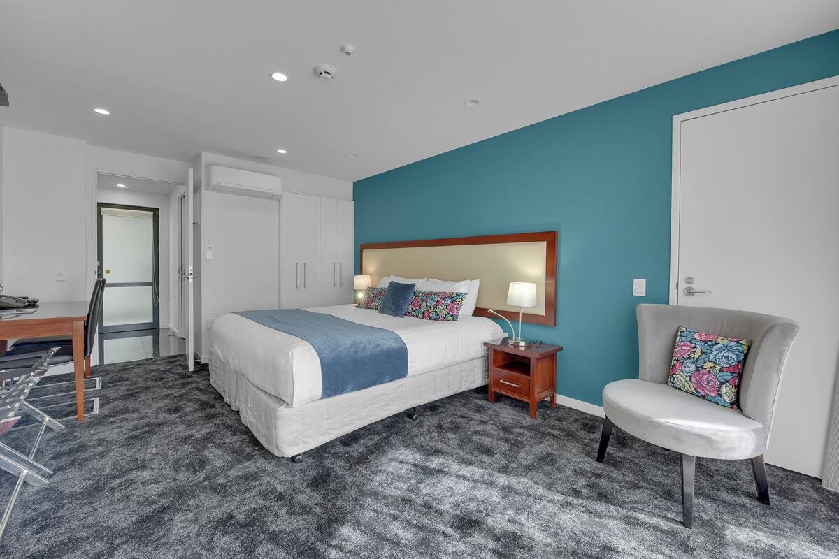 A modern hotel room with a large bed, a desk, and a chair.