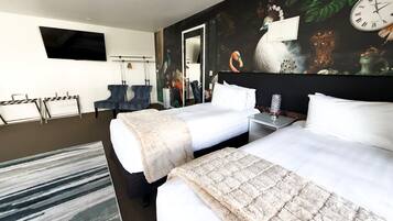 Ett hotellrum med två sängar, en platt-TV, en tavla och en väckarklocka på väggen.