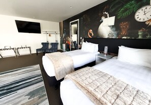 A hotel room with two beds, a flat-screen TV, a painting, and a clock on the wall. - DeLorenzo's Studio Apartments (Nelson)