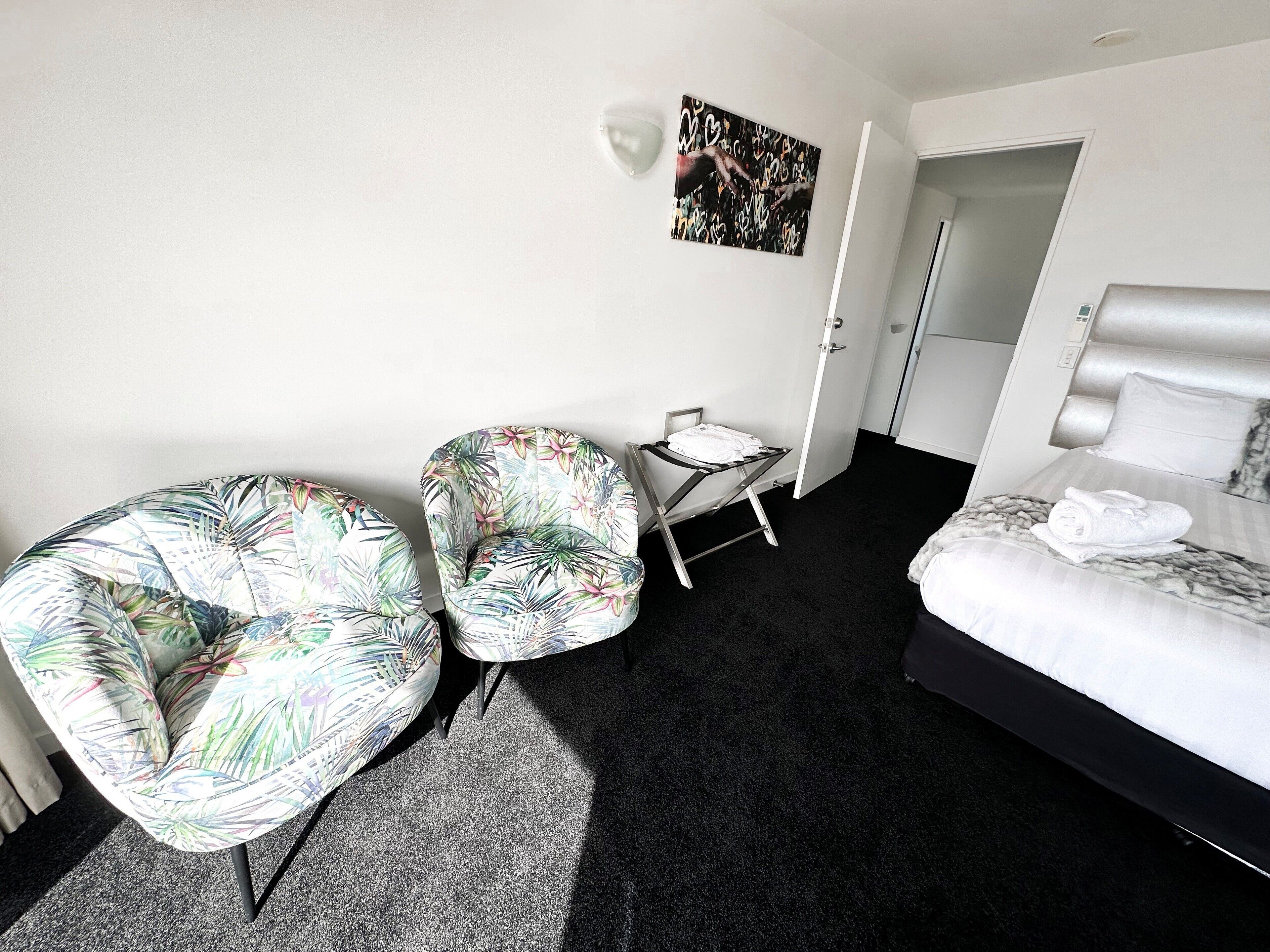 A hotel room with a bed, two chairs, a small table, and a painting on the wall.