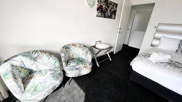 A hotel room with a bed, two chairs, a small table, and a painting on the wall.
