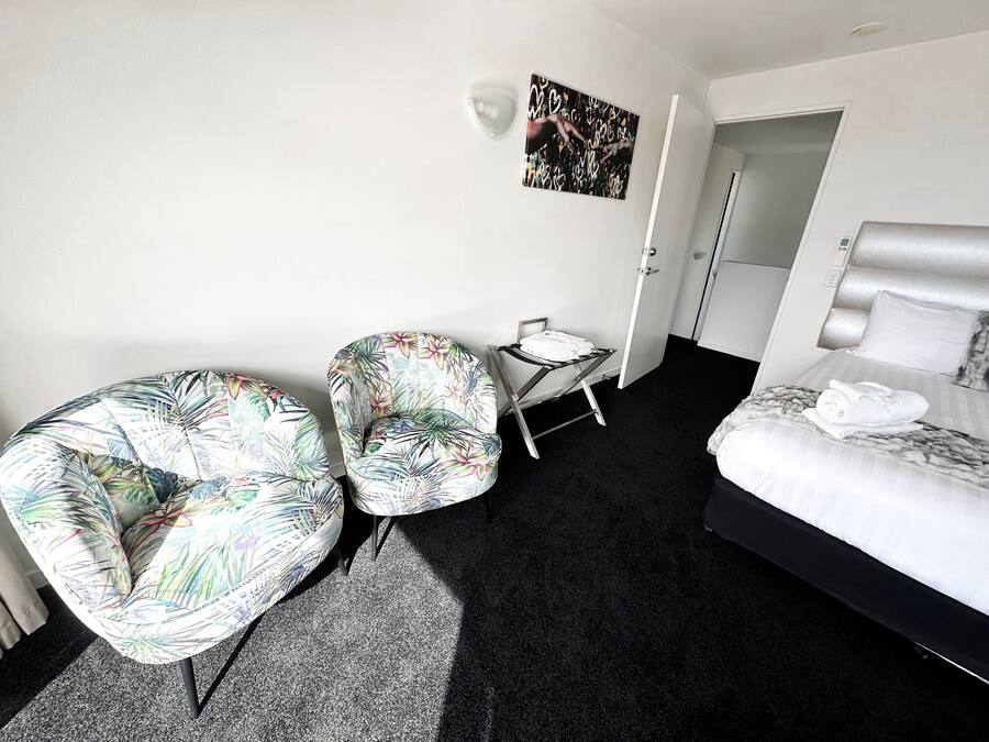 A hotel room with a bed, two chairs, a small table, and a painting on the wall.