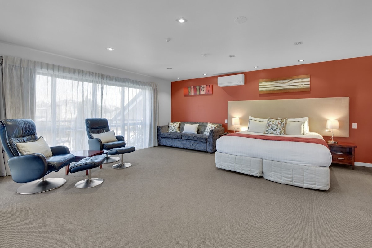 A hotel room with a large bed, two sofas, a coffee table, and a desk.