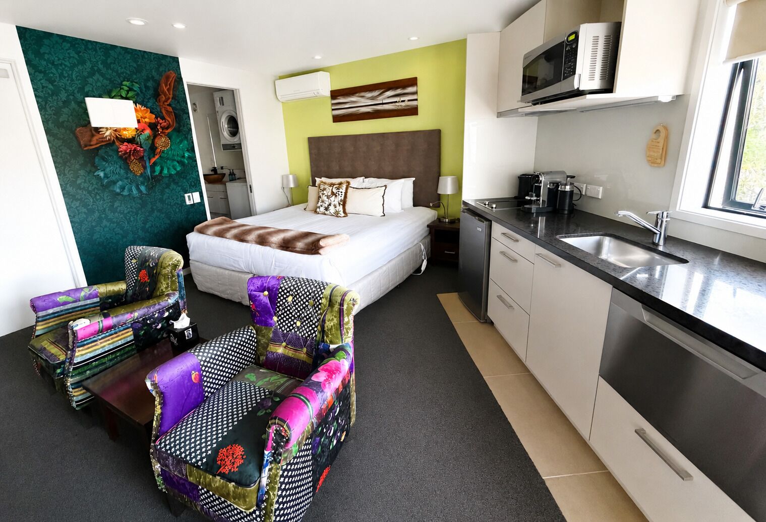 A compact hotel room with a bed, a kitchenette, a dining area, and a bathroom.