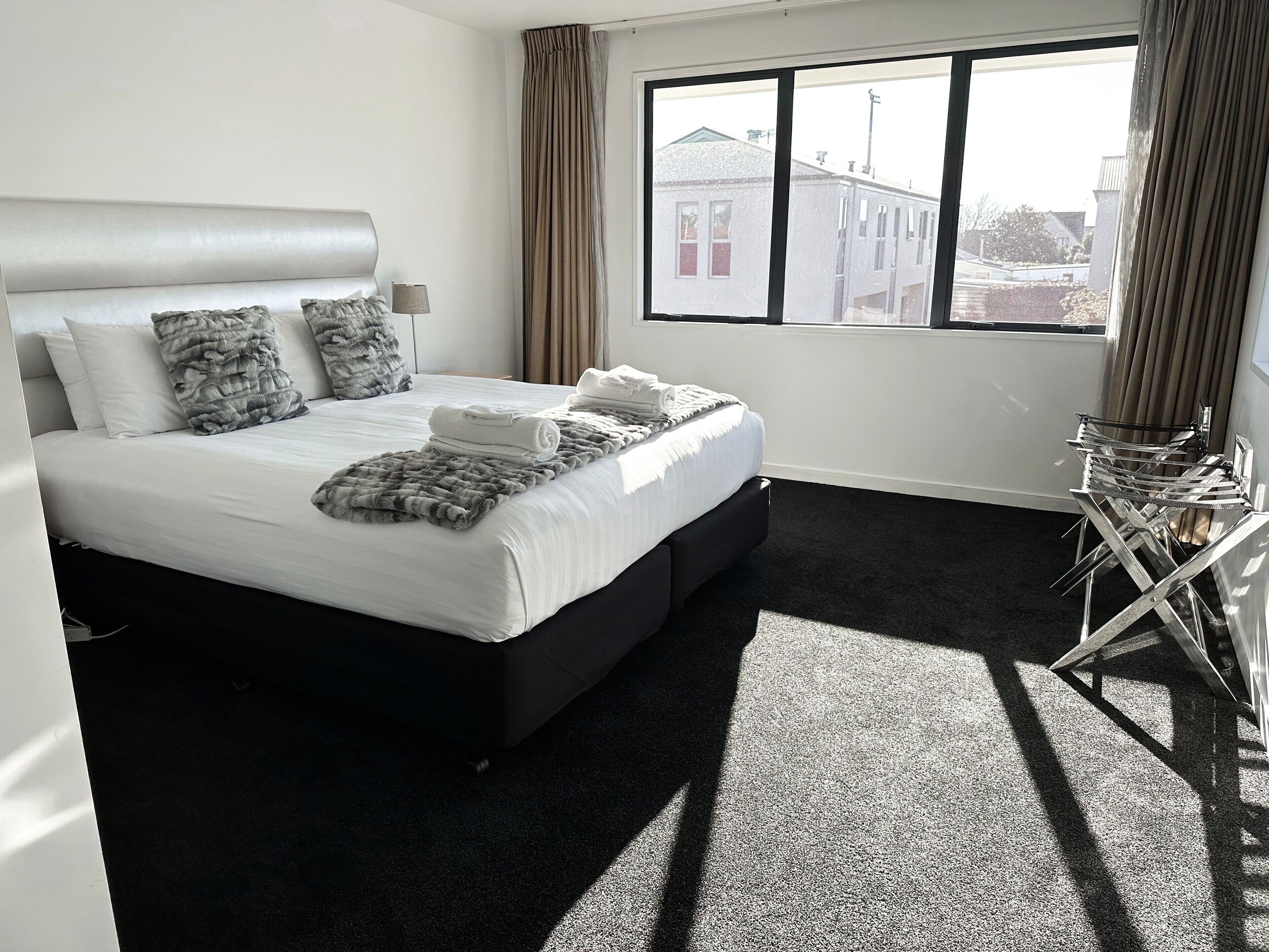Een moderne hotelkamer met een groot bed en uitzicht op gebouwen, plus een raam met gordijnen.