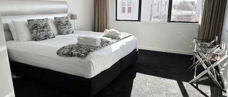 A modern hotel room with a large bed, a view of buildings outside, and a window with curtains.