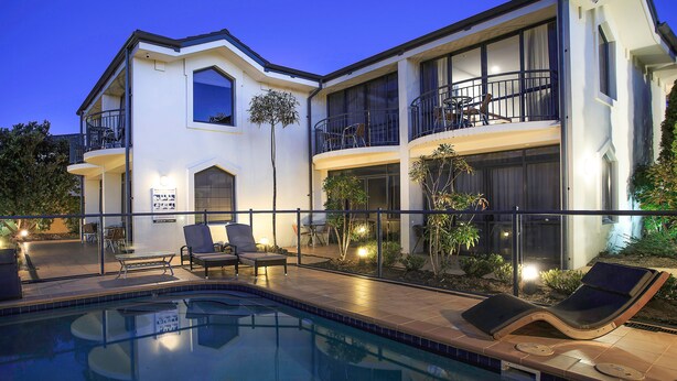 A modern two-story house with a swimming pool, outdoor seating, and a well-lit balcony. - DeLorenzo's Studio Apartments (Nelson)