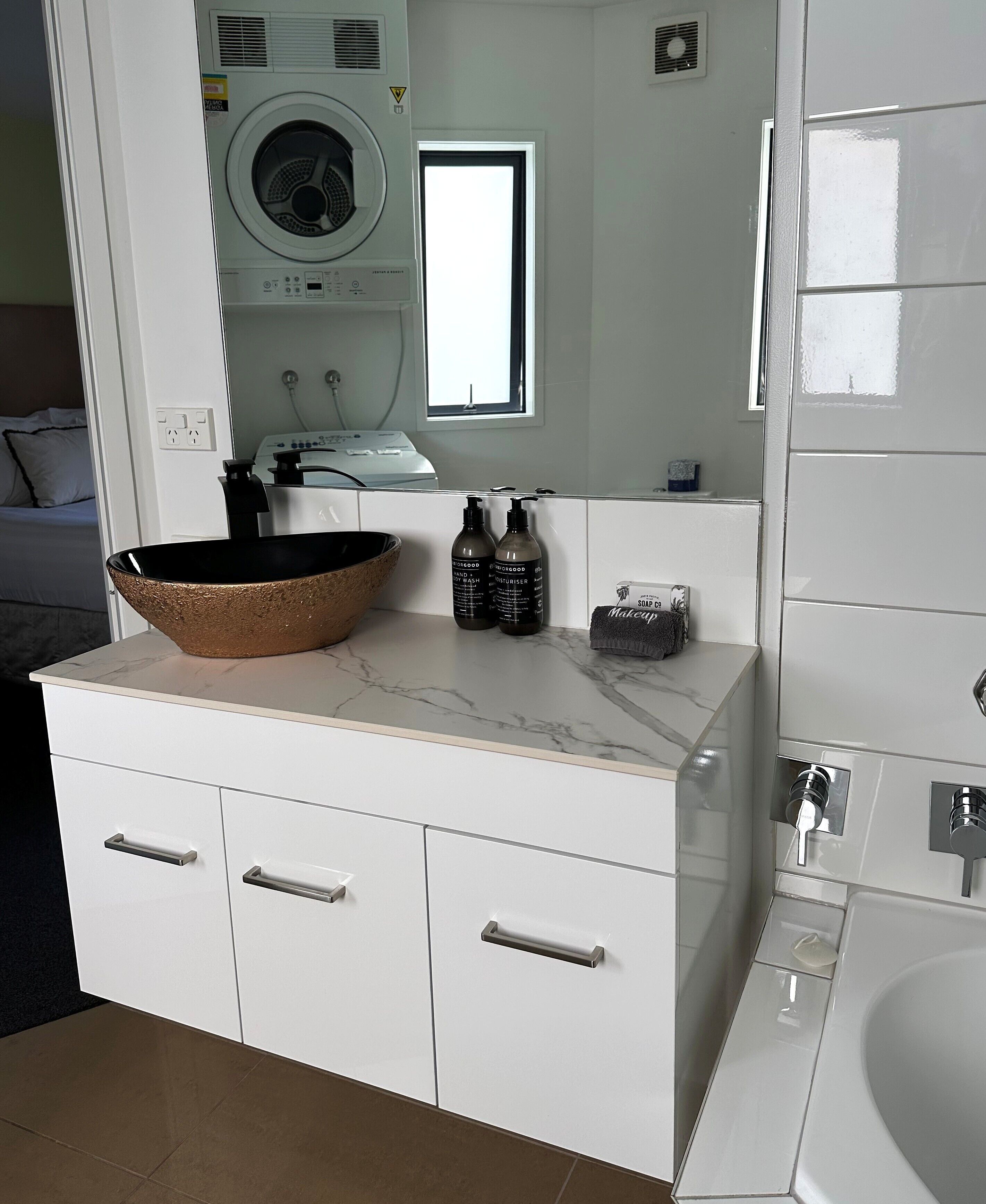 Un baño moderno con encimera de mármol, un espejo grande, una lavadora al fondo y una bañera.