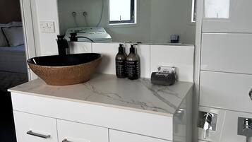 Un baño moderno con encimera de mármol, un espejo grande, una lavadora al fondo y una bañera.