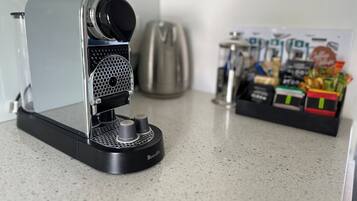 A Breville espresso machine on a kitchen counter with a coffee maker and a box of coffee pods in the background.
