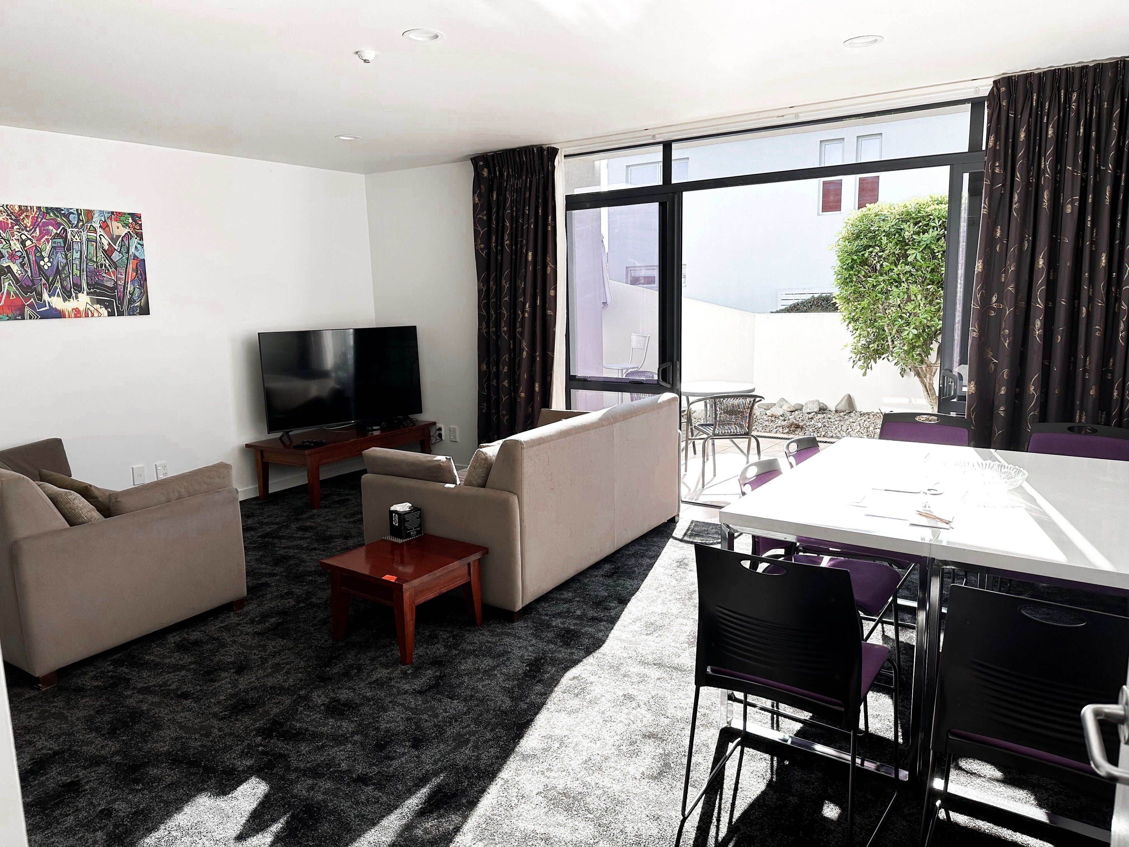 A modern living room with a sofa set, a coffee table, a TV, and a dining area with chairs and a table.