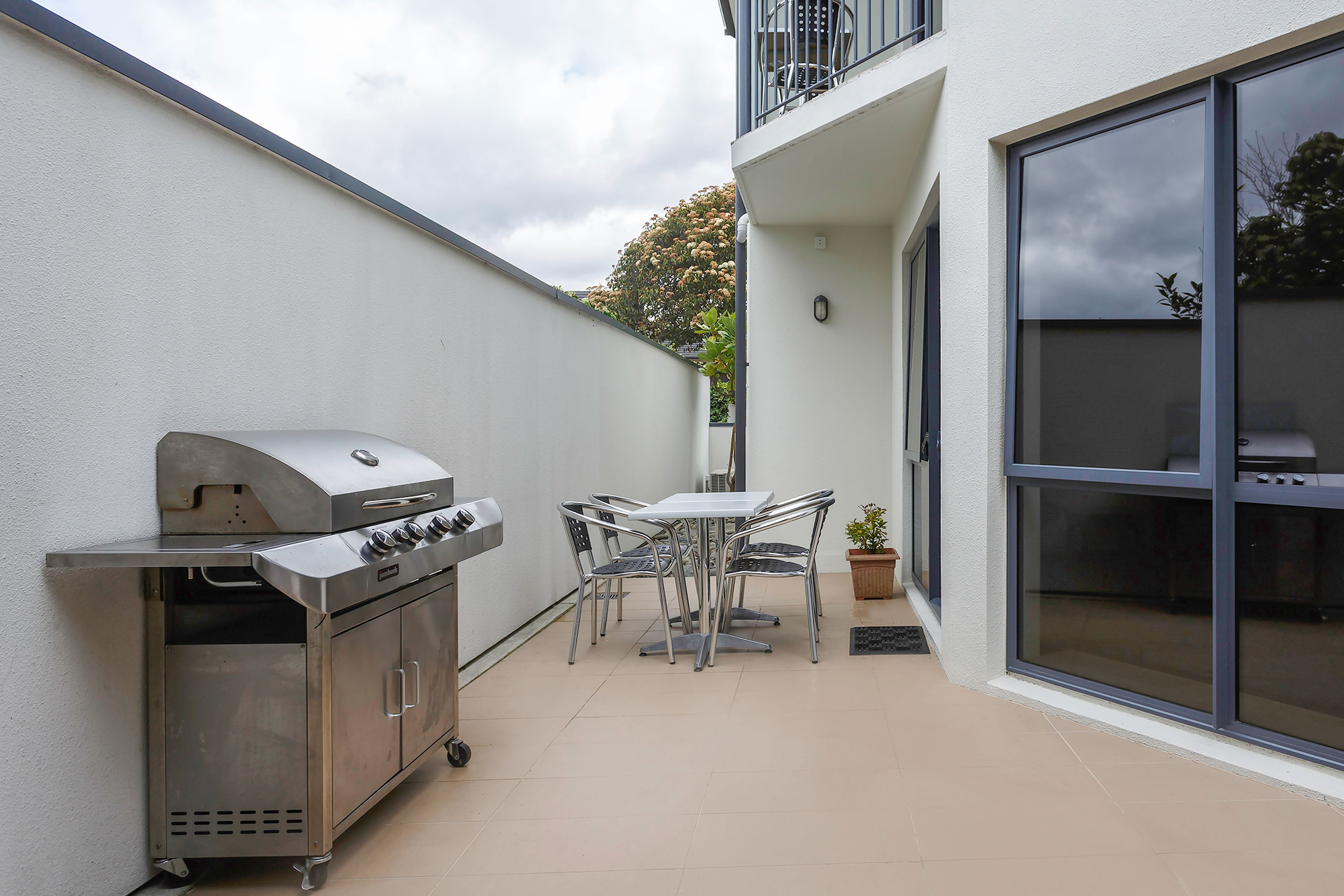 A patio with a stainless steel grill, a table, and chairs.