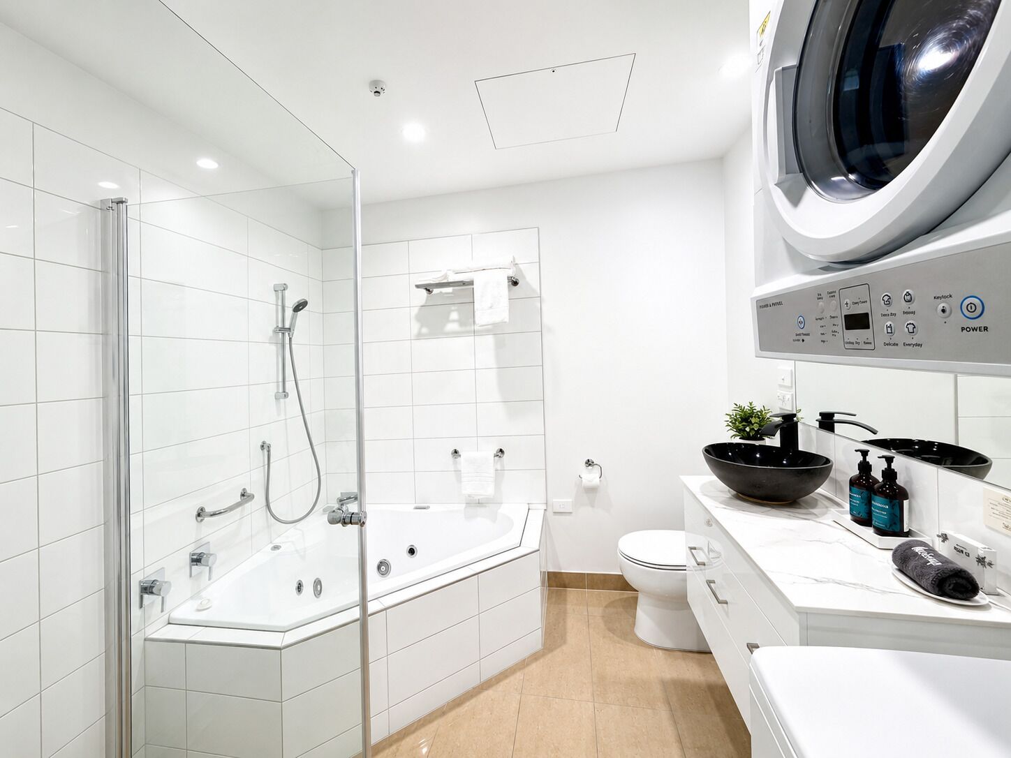 A modern bathroom with a glass-enclosed shower, a white toilet, and a built-in washing machine.