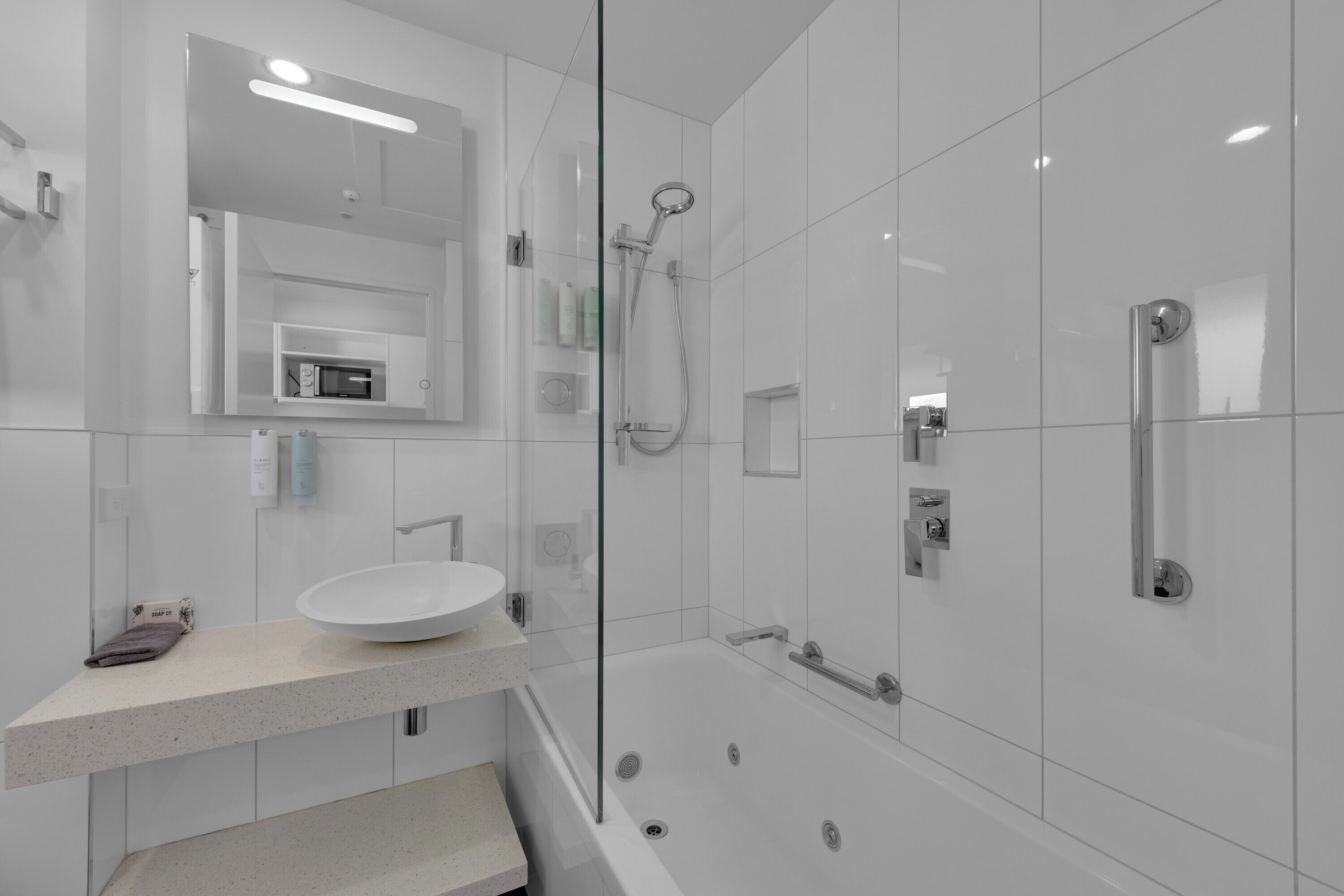 Un baño moderno con cabina de ducha de vidrio, un lavabo blanco y un espejo sobre el lavabo.