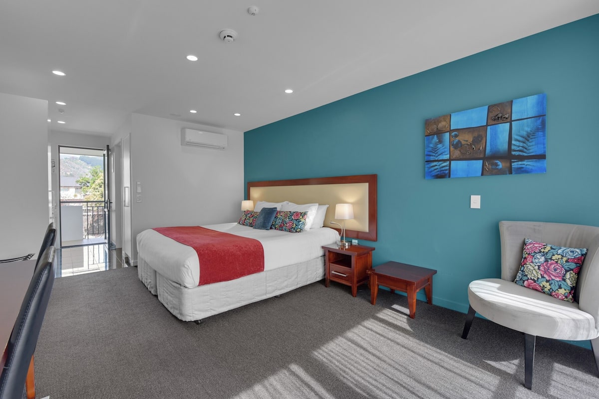 A modern hotel room with a large bed, a desk, a chair, and a view of the outdoors.