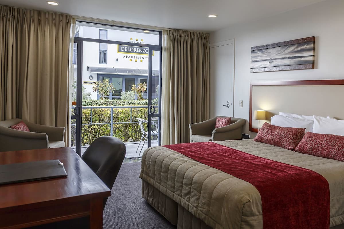 A hotel room with a bed, two chairs, a desk, and a view of the outside.