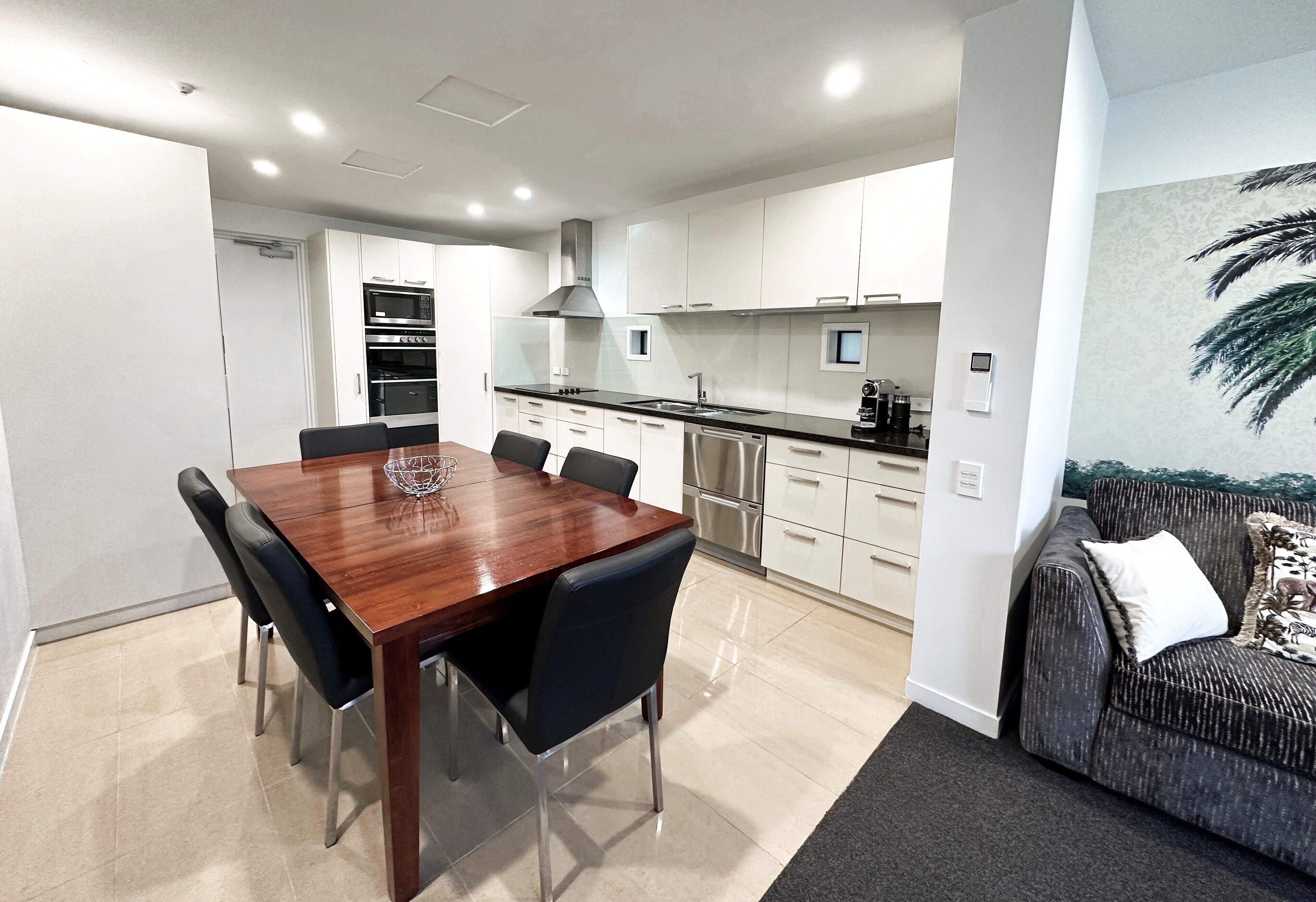 A modern kitchen with white cabinets, stainless steel appliances, and a dining area with a wooden table and chairs.