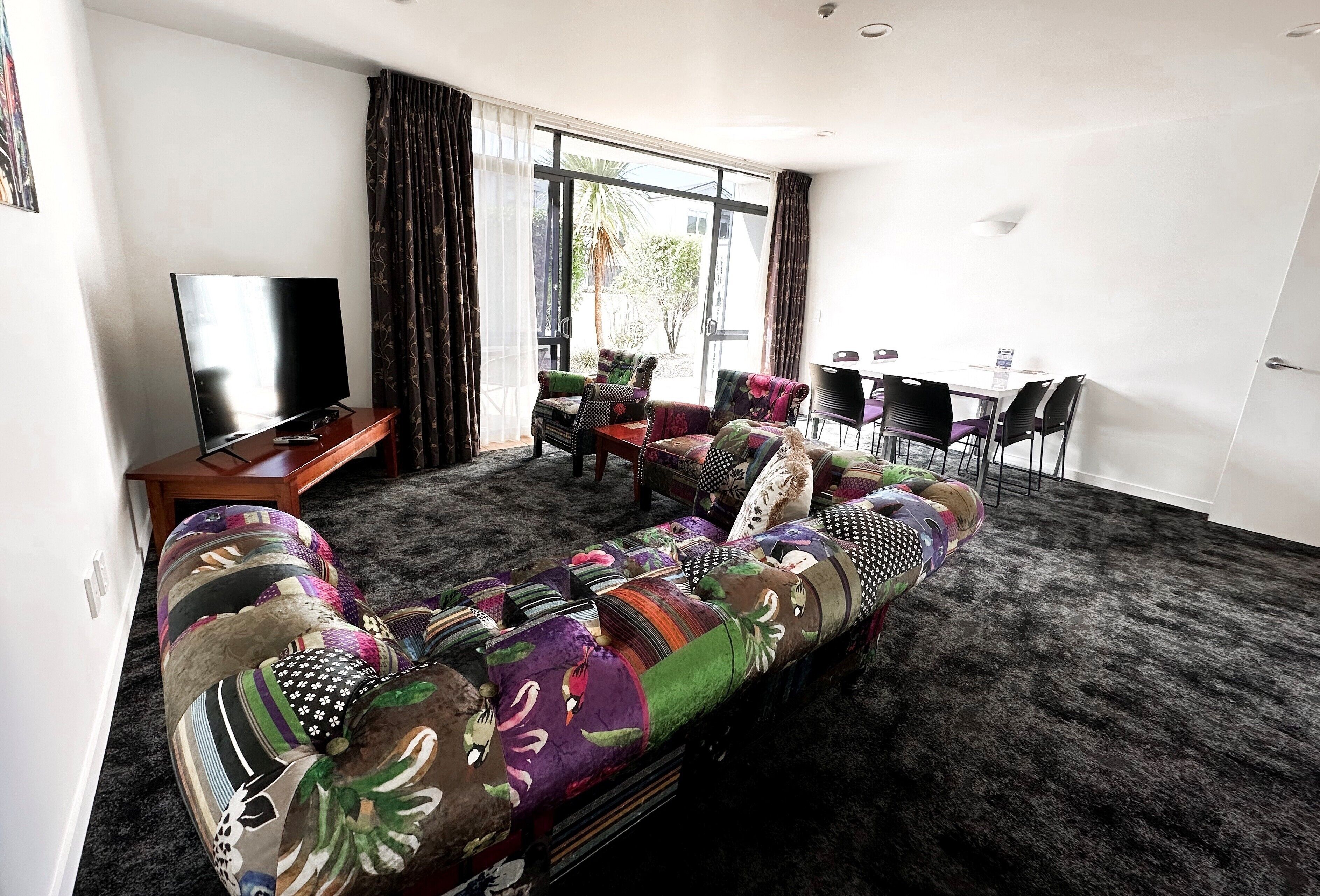 A living room with a large sofa, a flat-screen TV, and a dining area with chairs and a table.