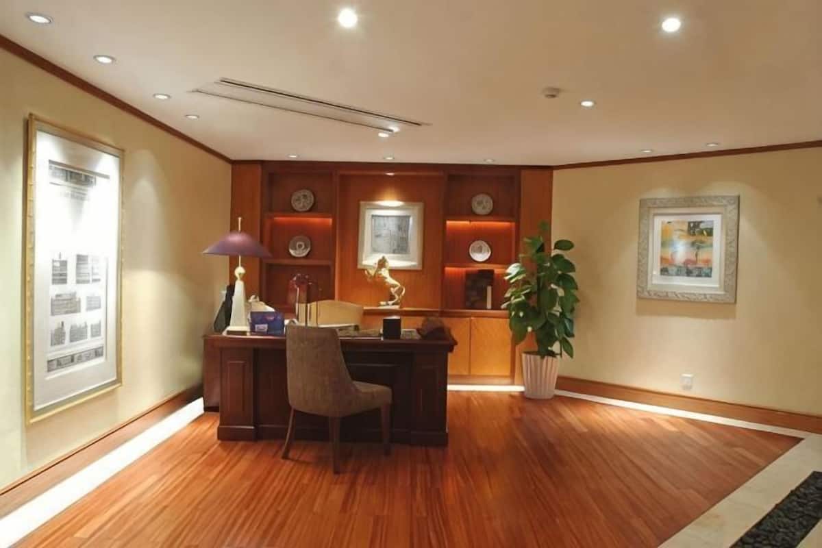 A room with a wooden desk, chair, framed pictures, and a potted plant.