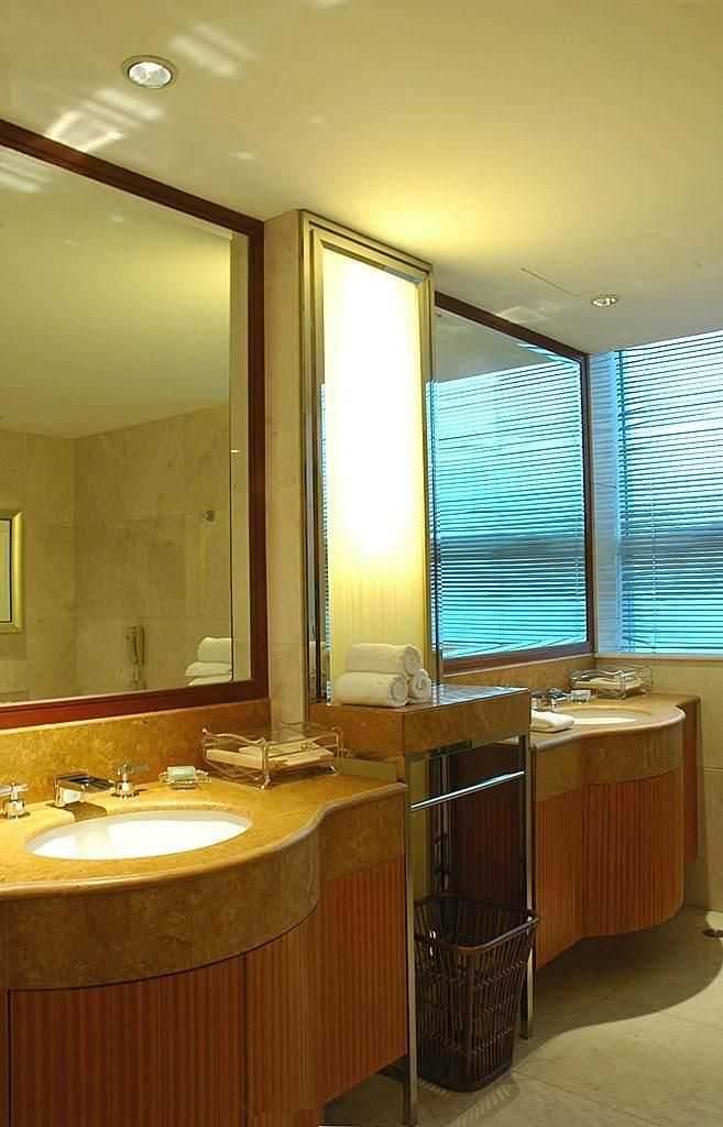 Un baño de hotel con dos lavamanos, un espejo grande y una ventana con persianas.