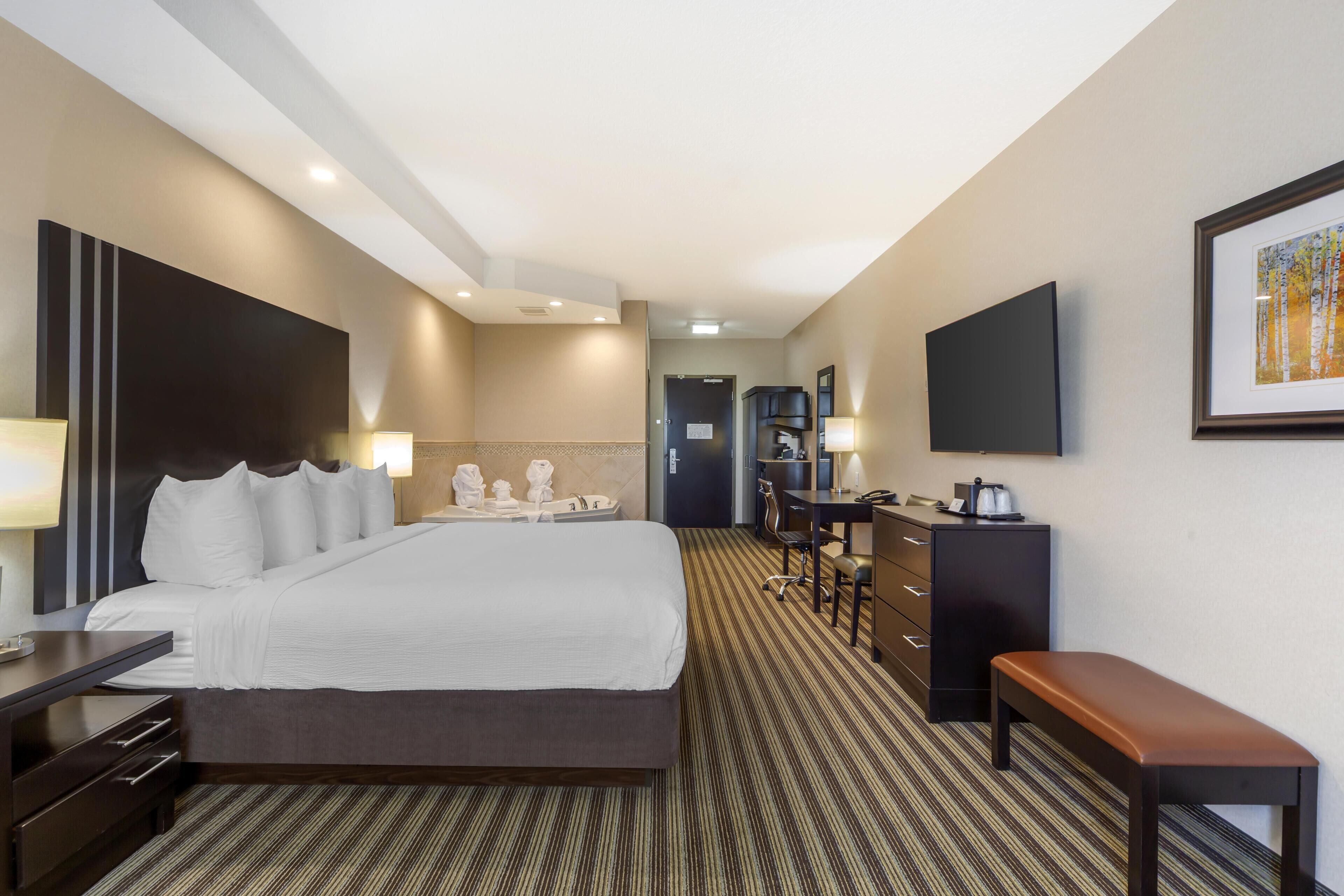 Une chambre d’hôtel avec un grand lit, un bureau, une chaise, un banc et un téléviseur fixé au mur.