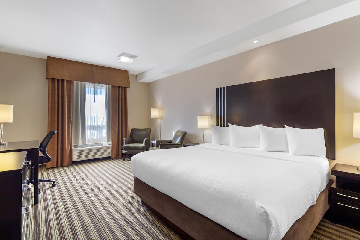 A hotel room with a large bed, two chairs, a desk, and a window with curtains.