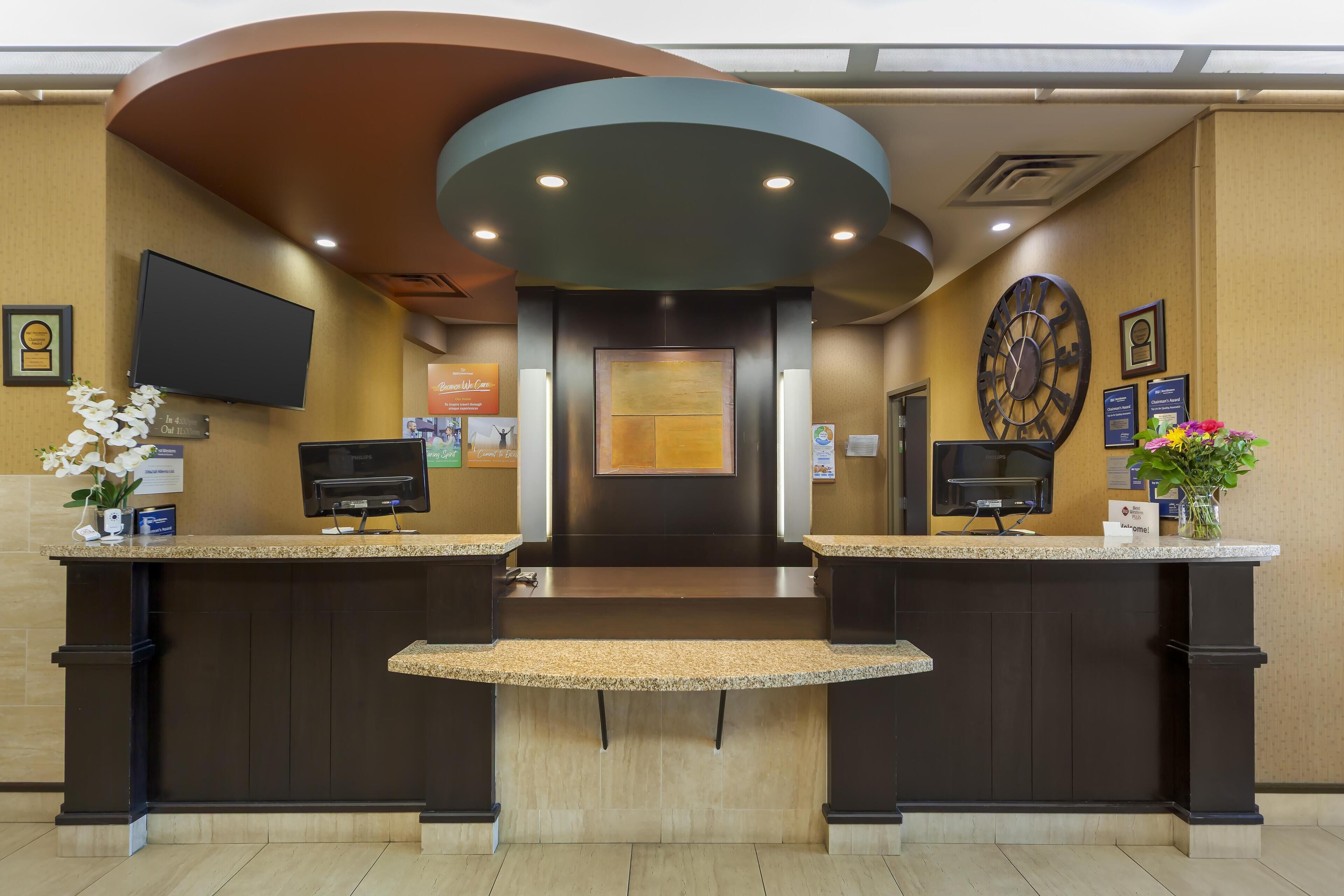 A reception area with a modern design, featuring a large clock, a flat-screen TV, and a reception desk with a digital display.