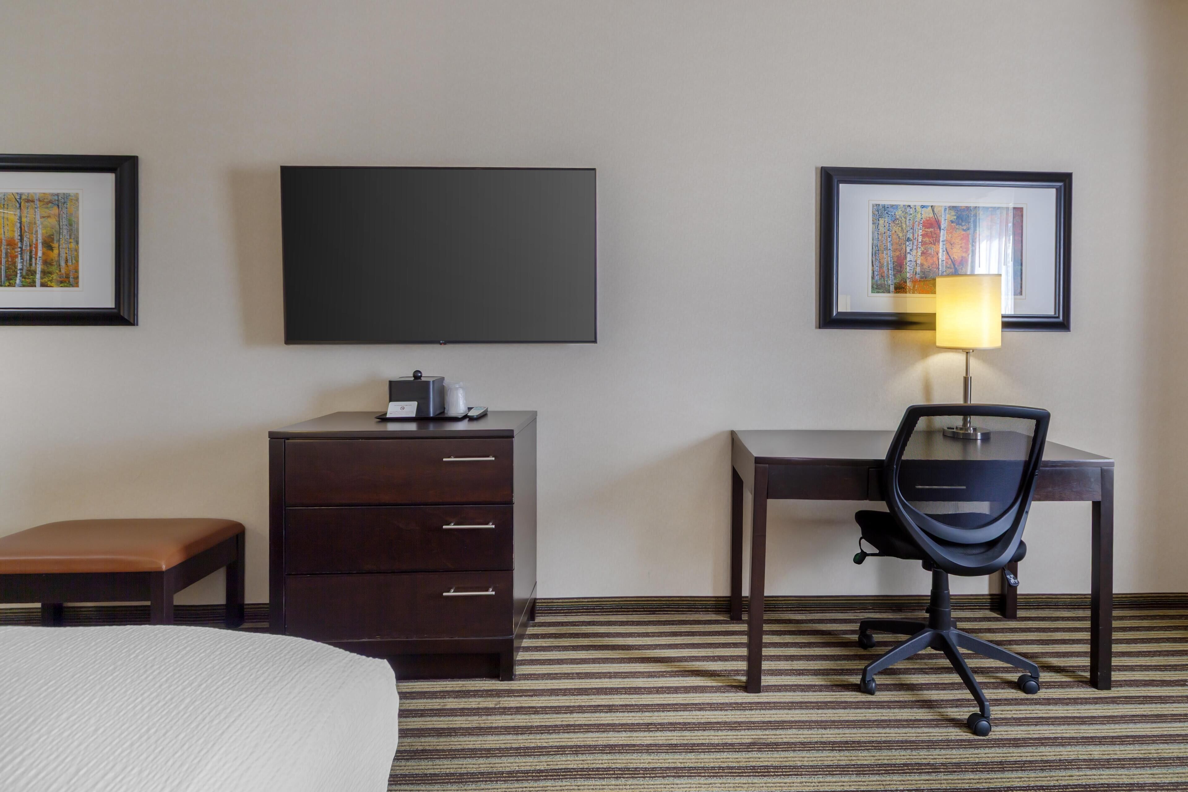 Een hotelkamer met een bed, een bureau met stoel, een dressoir, een flatscreen televisie en ingelijste kunstwerken aan de wanden.