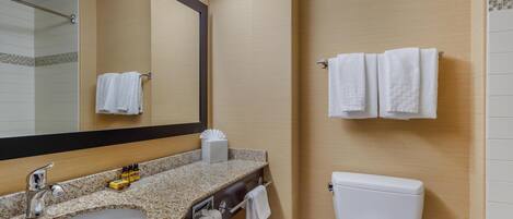 A bathroom with a granite countertop sink, a mirror, a toilet, and two towels hanging on the wall.