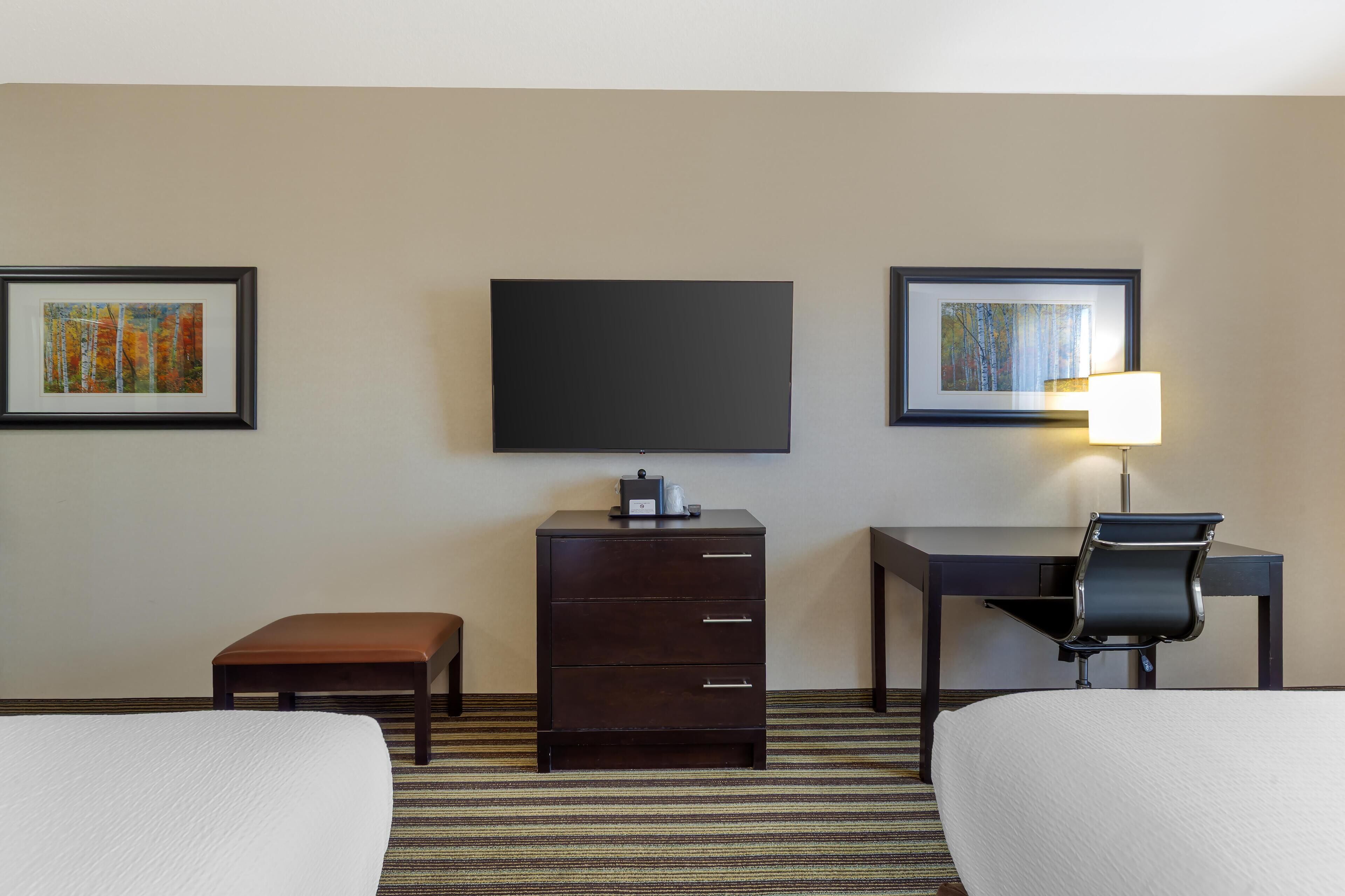 Habitación de hotel con dos camas, un escritorio, una silla, un aparador y un televisor de pantalla plana en la pared.