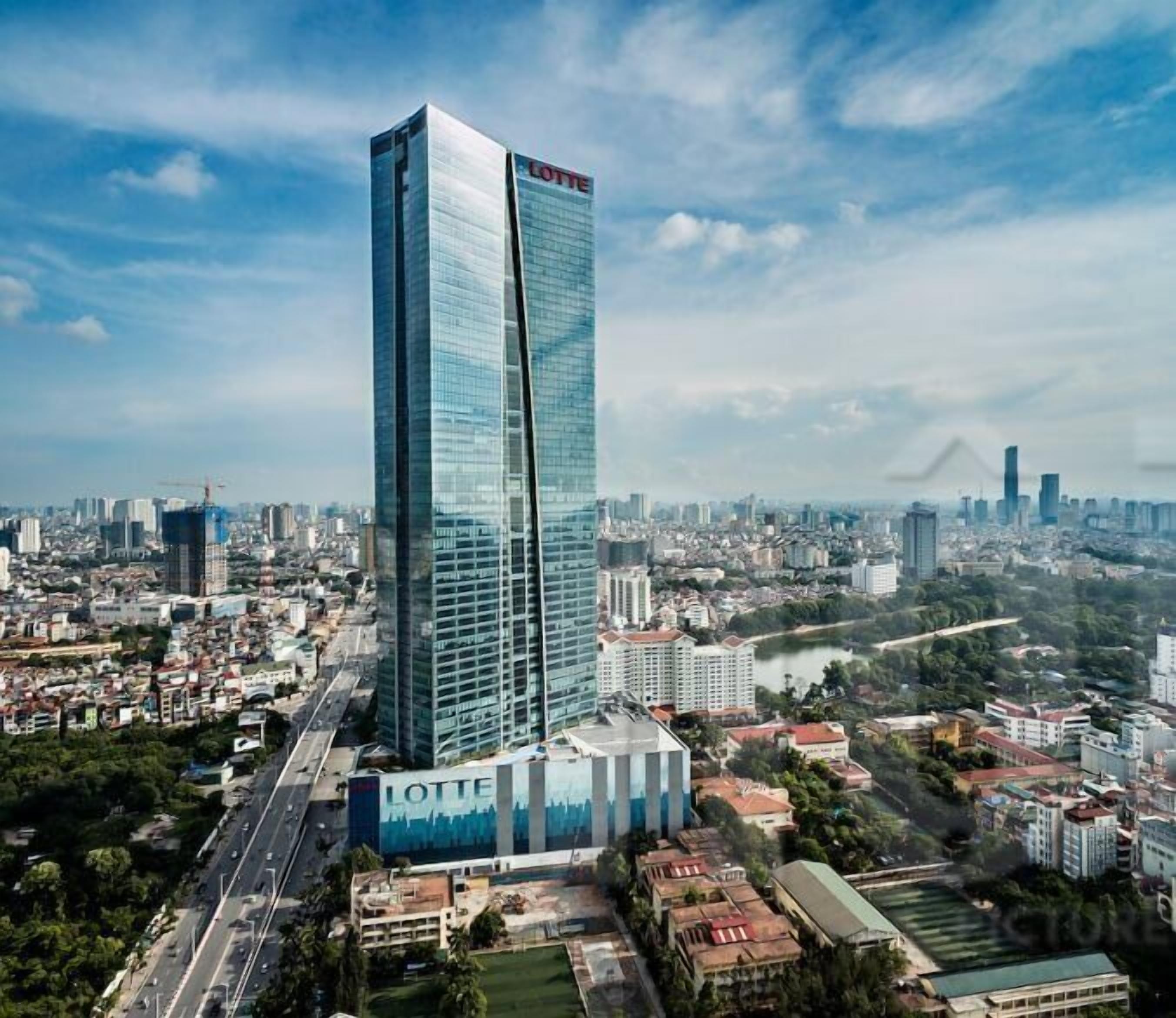 Un edifici alt amb un cartell ben visible de 'LOTTE', envoltat d'un paisatge urbà amb diversos edificis i un riu al fons.