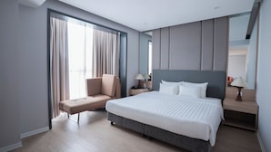 Habitación de hotel moderna con una cama grande, zona de estar y mesita de noche con lámpara.
