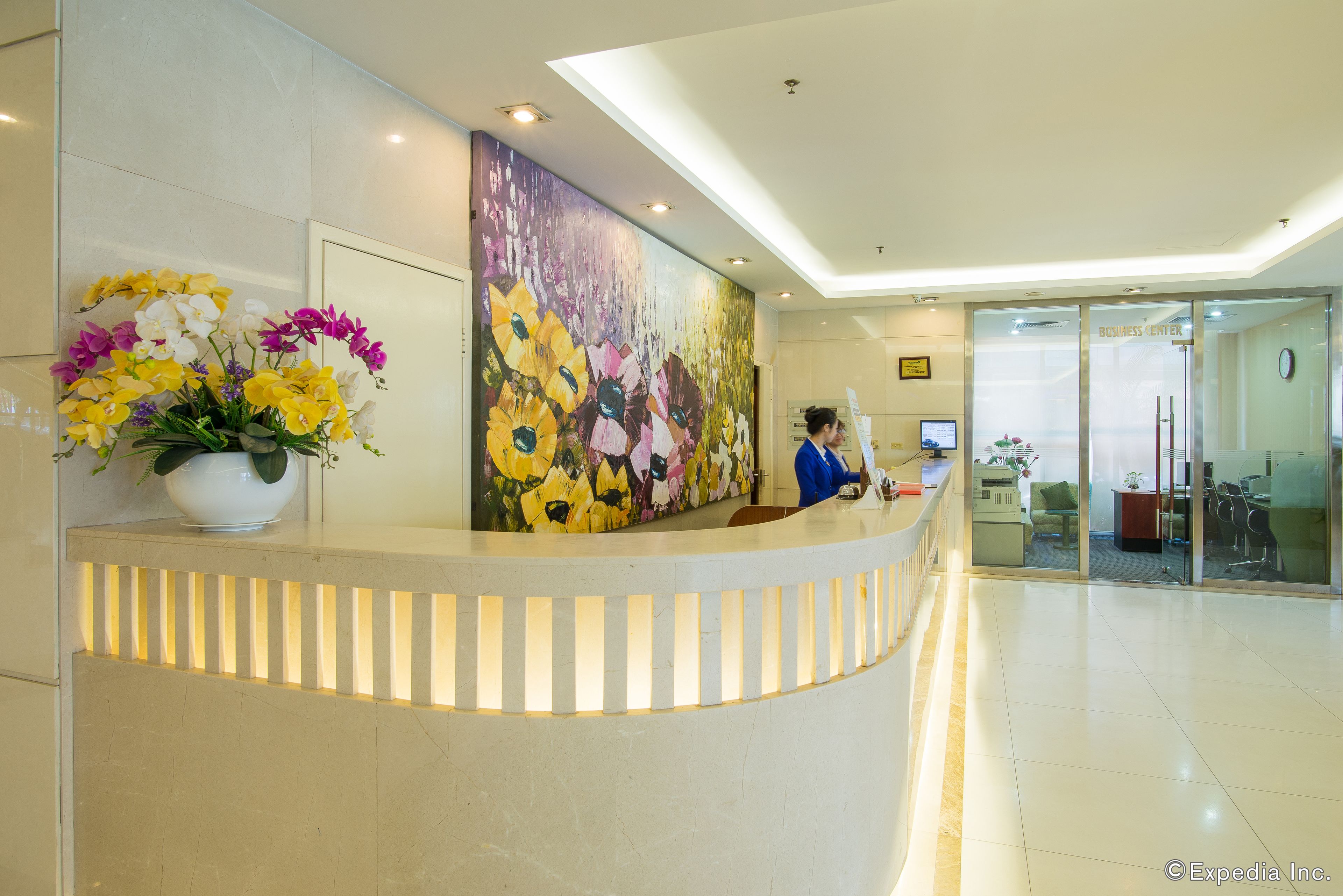Un área de recepción con un mostrador curvo, un gran mural floral y una puerta de vidrio que da a un espacio de oficina.
