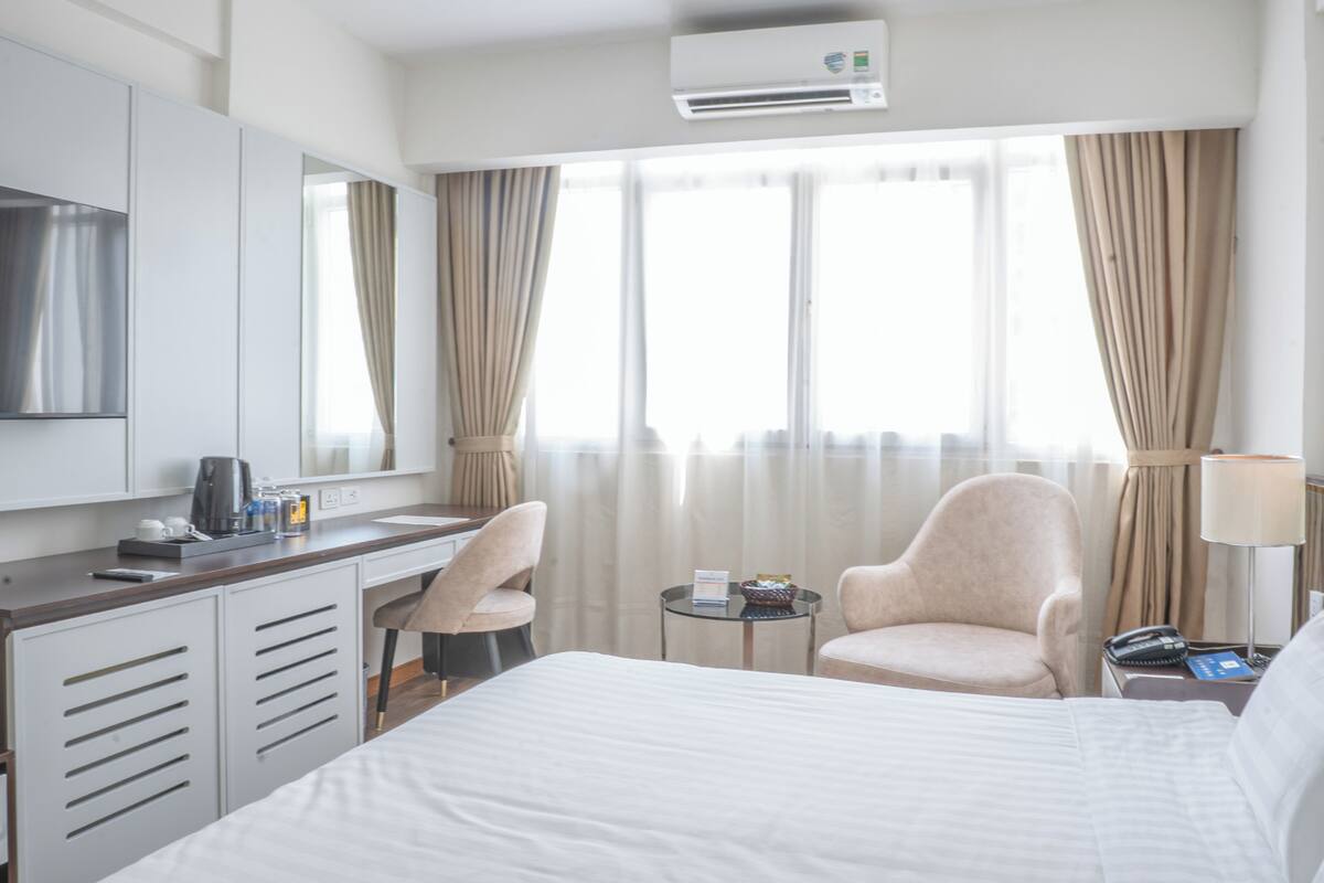 Une chambre d’hôtel avec un lit, un bureau, une chaise, une petite table et une fenêtre avec des rideaux.
